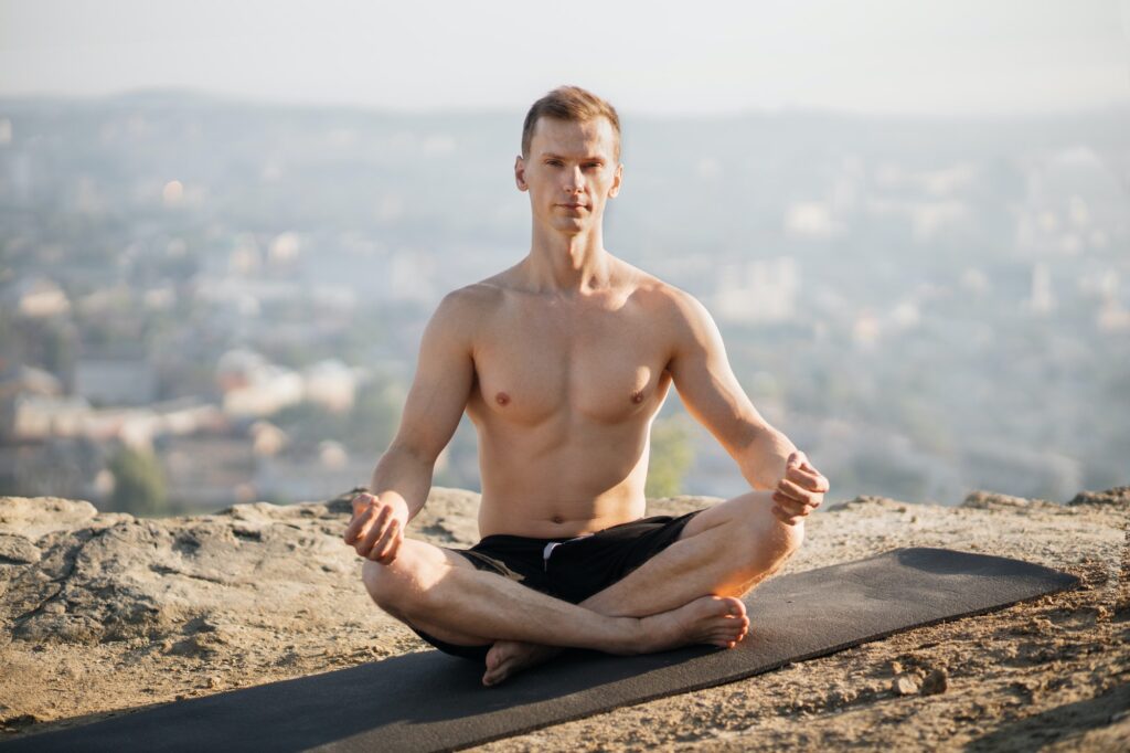 Relaxed shirtless man practising yoga on fresh air, meditating